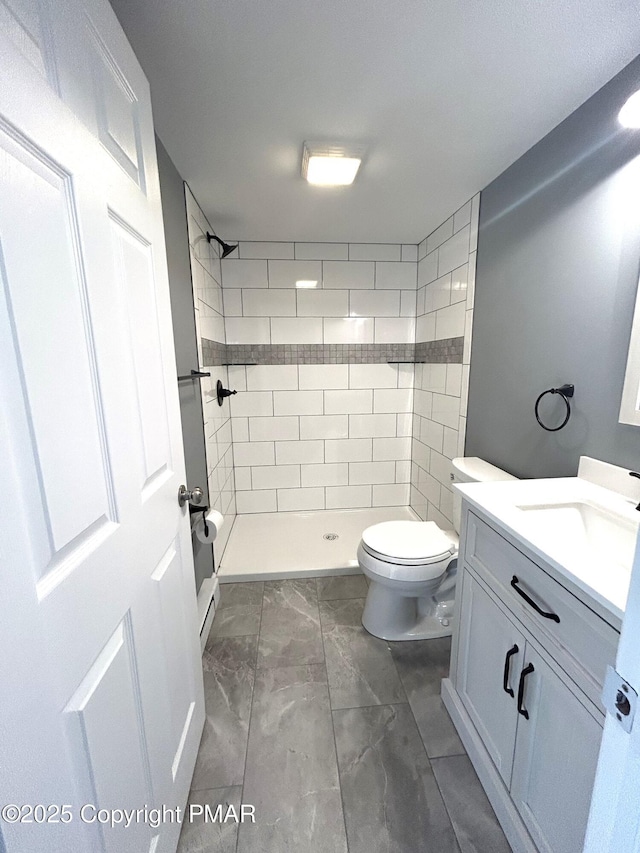 bathroom with a tile shower, vanity, and toilet