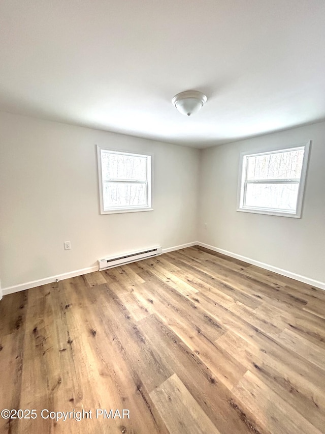 empty room featuring a baseboard radiator, baseboards, and wood finished floors