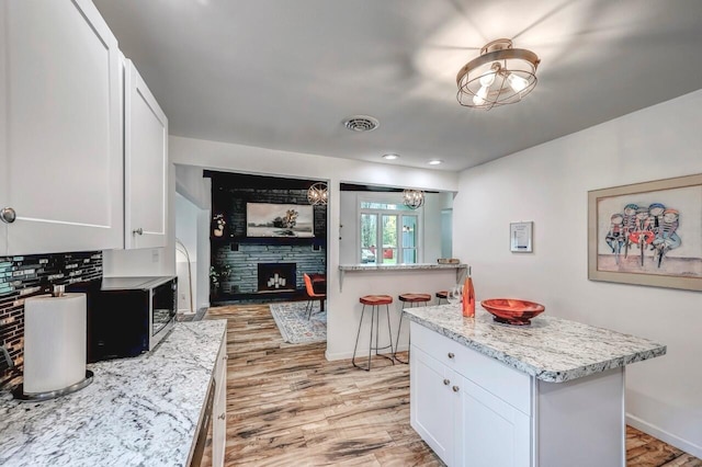 134 Altemose Rd, Pocono Lake, PA 18347 - kitchen with a fireplace, stainless steel microwave, light wood finished floors, and white cabinetry