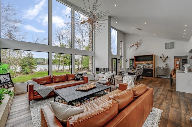 living room featuring a water view, high vaulted ceiling, hardwood / wood-style floors, and visible vents