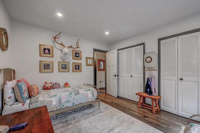 bedroom with two closets, recessed lighting, and wood finished floors