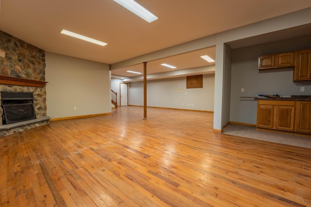 unfurnished living room featuring a stone fireplace, light wood-style flooring, baseboards, heating unit, and stairway