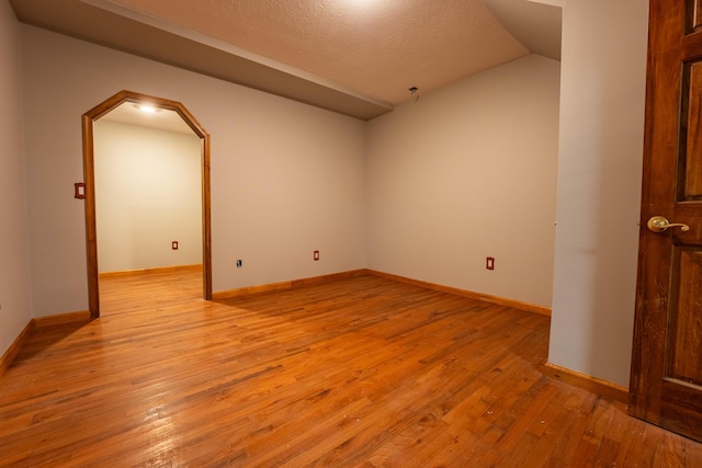 unfurnished room featuring baseboards, a textured ceiling, arched walkways, light wood-style flooring, and vaulted ceiling