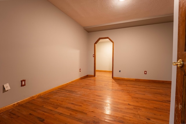spare room with arched walkways, a textured ceiling, baseboards, light wood-type flooring, and vaulted ceiling