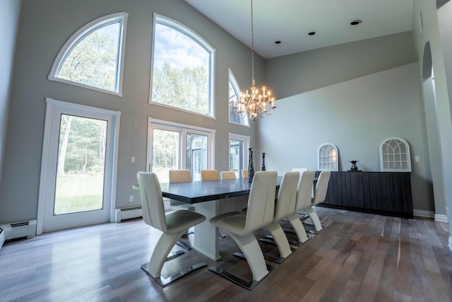 dining space featuring a baseboard heating unit, a towering ceiling, wood finished floors, and a chandelier