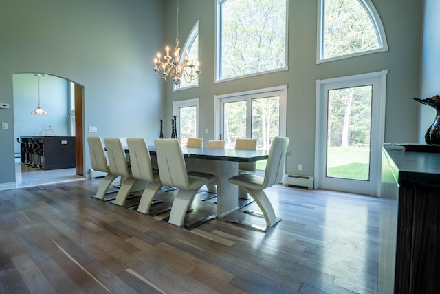 dining room with wood finished floors, an inviting chandelier, baseboard heating, and a towering ceiling