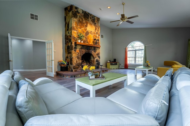 living room featuring a stone fireplace, a ceiling fan, baseboards, wood finished floors, and visible vents