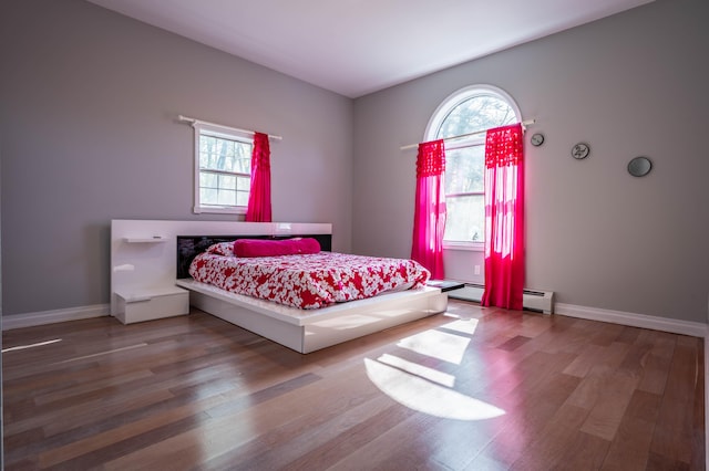 bedroom featuring baseboards, multiple windows, a baseboard heating unit, and wood finished floors