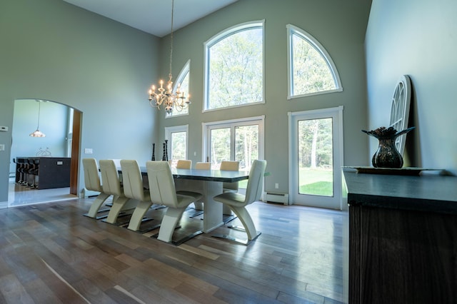 dining room featuring a high ceiling, arched walkways, a chandelier, wood finished floors, and a baseboard heating unit