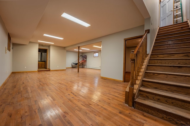finished basement featuring stairway, baseboards, a baseboard radiator, and wood-type flooring