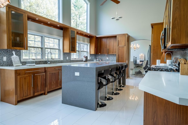 kitchen with range with gas stovetop, decorative backsplash, a kitchen breakfast bar, a high ceiling, and brown cabinets