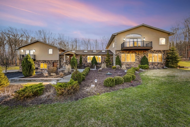 374 Packer Dr, Weatherly, PA 18255 - back of house at dusk with stucco siding, stone siding, a lawn, and a balcony