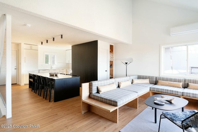 living room with a towering ceiling, a wall mounted AC, and light wood-type flooring