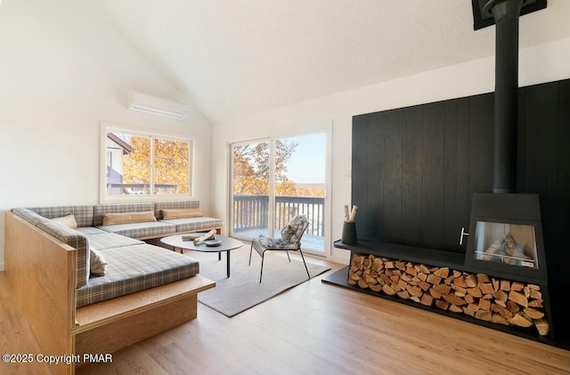 living room featuring a wall unit AC, a wood stove, wood finished floors, and high vaulted ceiling