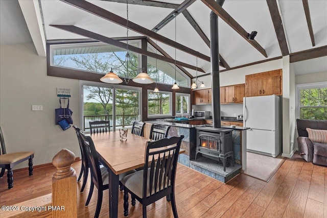 dining area featuring light wood-style flooring, beamed ceiling, a wood stove, high vaulted ceiling, and a notable chandelier