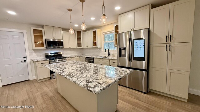 kitchen featuring stainless steel appliances, hanging light fixtures, a center island, and light stone counters