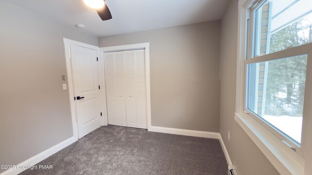 unfurnished bedroom with multiple windows, ceiling fan, dark carpet, and a closet