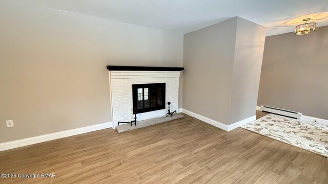 unfurnished living room with an inviting chandelier, a baseboard heating unit, a brick fireplace, and light wood-type flooring