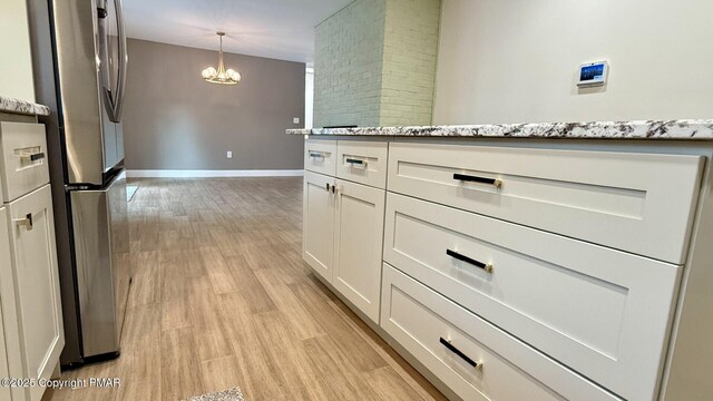 kitchen with stainless steel fridge, light hardwood / wood-style flooring, white cabinetry, light stone counters, and decorative light fixtures