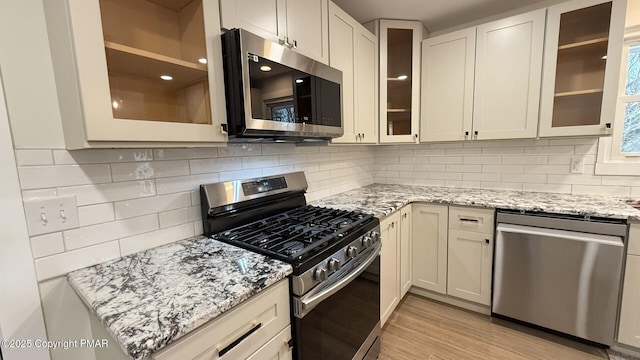 kitchen with appliances with stainless steel finishes, white cabinetry, light stone counters, decorative backsplash, and light wood-type flooring