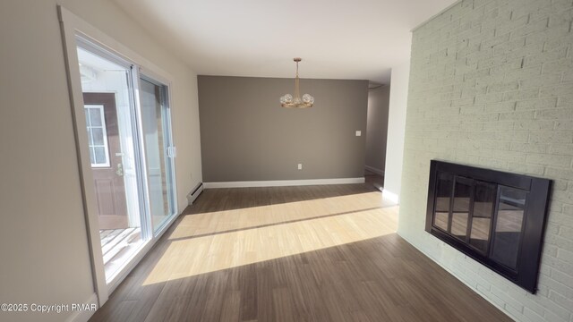 unfurnished dining area featuring an inviting chandelier, dark wood-type flooring, a fireplace, and a baseboard radiator