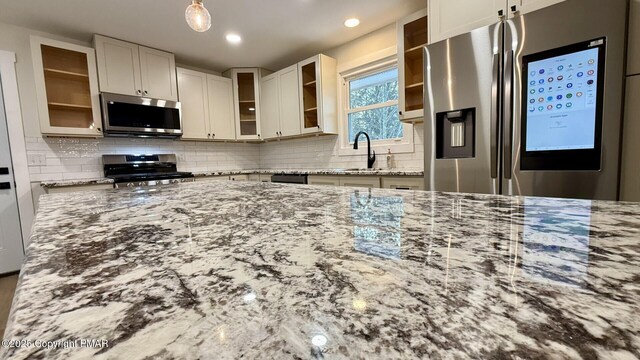 kitchen with appliances with stainless steel finishes, tasteful backsplash, sink, white cabinets, and light stone countertops