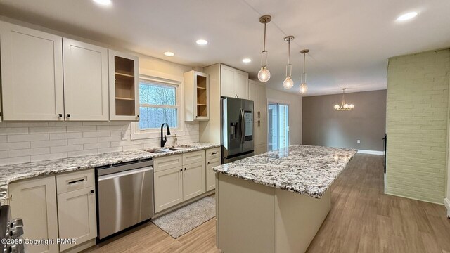 kitchen with sink, a kitchen island, light stone countertops, and appliances with stainless steel finishes