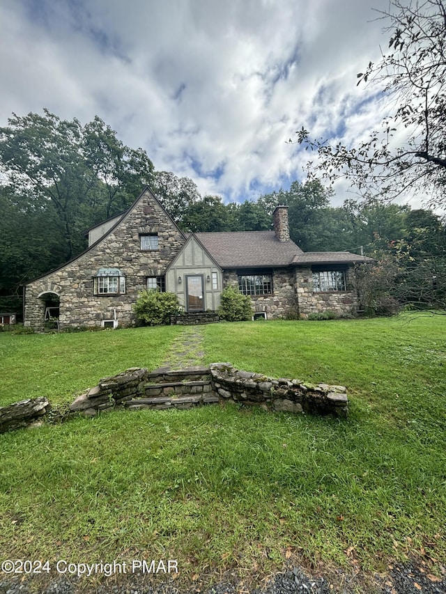 view of front of home featuring stone siding, a chimney, and a front lawn