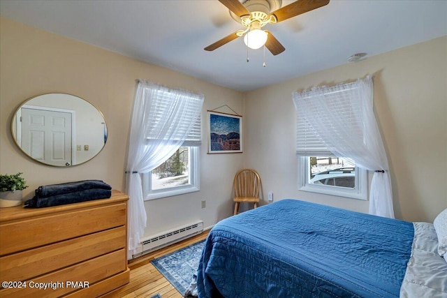 bedroom with light wood-style floors, multiple windows, baseboard heating, and a ceiling fan