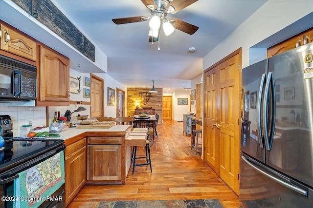 kitchen with tasteful backsplash, brown cabinetry, light wood-style flooring, a peninsula, and black appliances