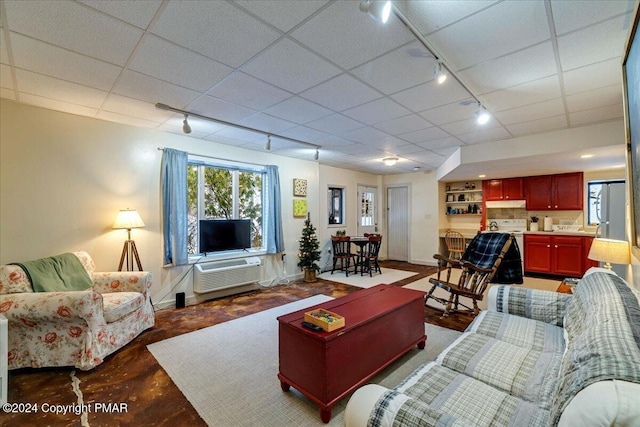 living area featuring a paneled ceiling, baseboards, track lighting, and a wall mounted air conditioner