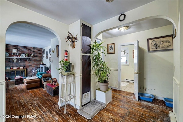 hall with visible vents, arched walkways, baseboards, wood-type flooring, and a baseboard heating unit