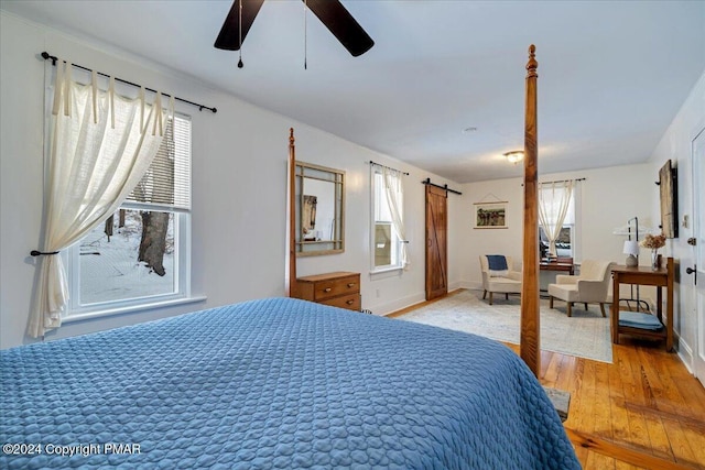 bedroom featuring a barn door, light wood-type flooring, a ceiling fan, and baseboards