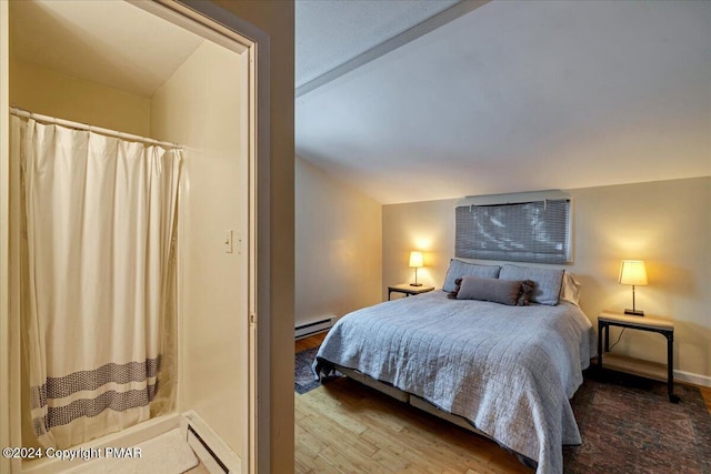 bedroom with baseboard heating, a baseboard heating unit, vaulted ceiling, wood finished floors, and baseboards