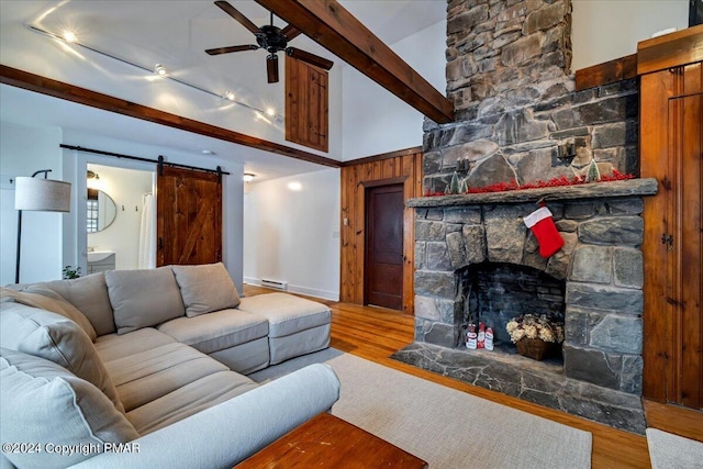 living room with a barn door, a ceiling fan, beamed ceiling, wood finished floors, and baseboard heating