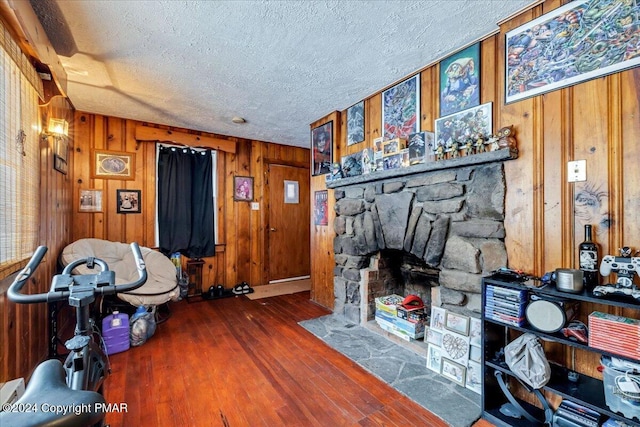 living room with a textured ceiling, a stone fireplace, hardwood / wood-style floors, and wood walls