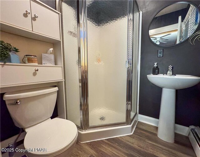 bathroom featuring hardwood / wood-style floors, baseboard heating, toilet, and a shower with door