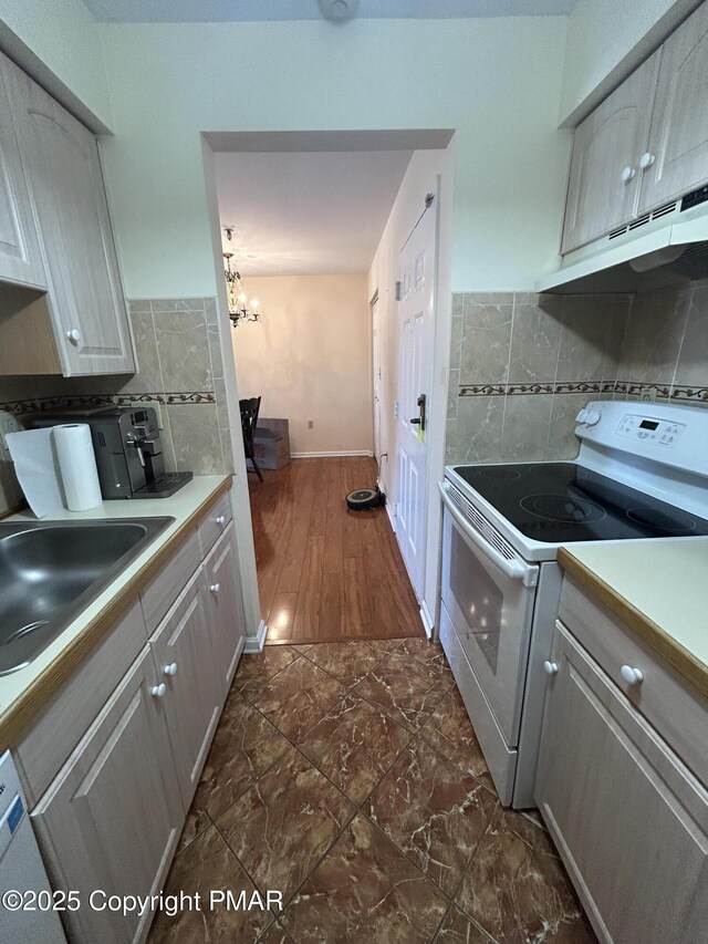 kitchen with white electric range oven, a sink, light countertops, under cabinet range hood, and backsplash