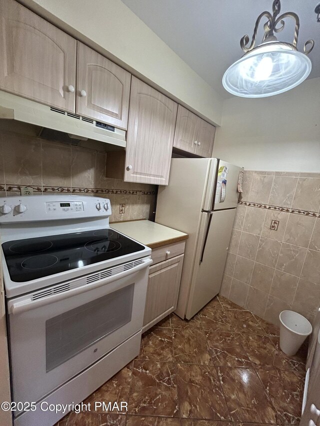 kitchen with white appliances, light brown cabinets, light countertops, under cabinet range hood, and tile walls