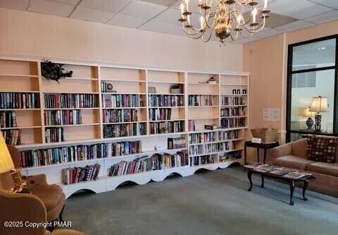 sitting room with bookshelves, a paneled ceiling, and a chandelier