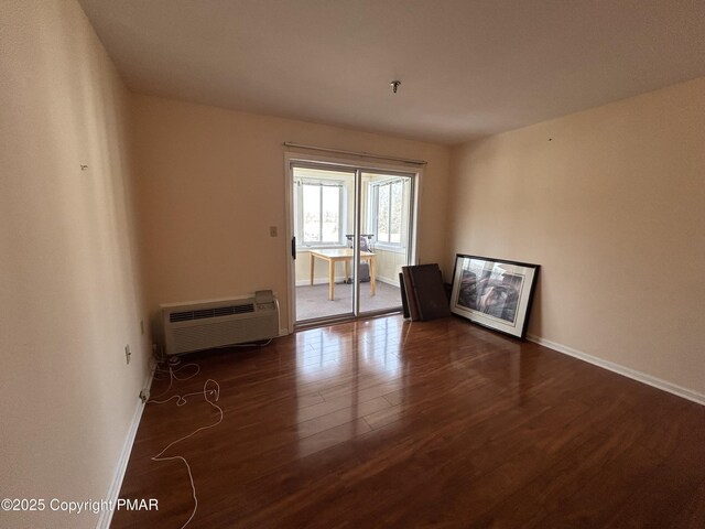 unfurnished room featuring a wall mounted air conditioner, baseboards, and wood finished floors