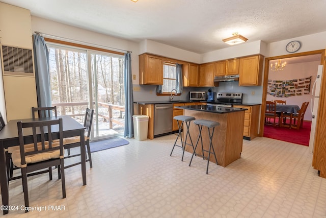 kitchen featuring under cabinet range hood, a kitchen island, a sink, appliances with stainless steel finishes, and light floors