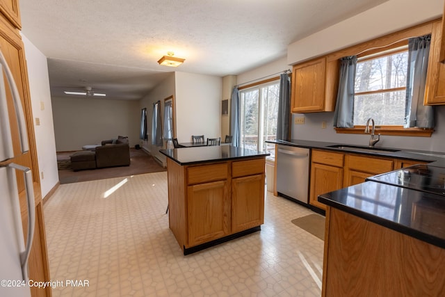 kitchen featuring a sink, stainless steel dishwasher, a center island, light floors, and dark countertops