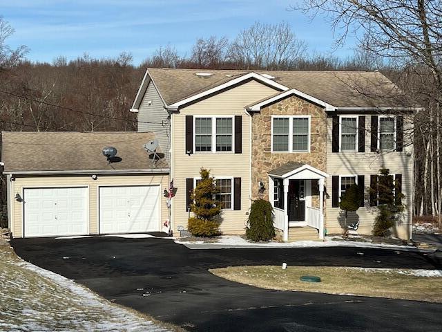 colonial-style house with stone siding, a garage, and driveway