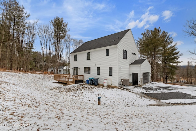 snow covered rear of property featuring a garage, a deck, and central air condition unit