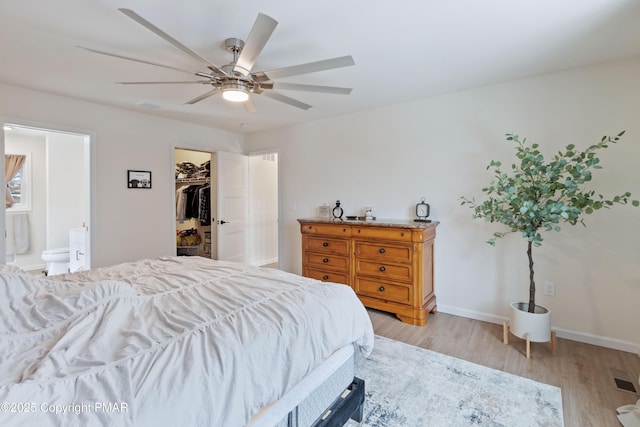 bedroom featuring ensuite bath, a spacious closet, light wood-type flooring, a closet, and ceiling fan