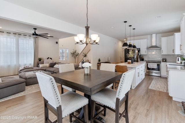 dining space with sink, ceiling fan with notable chandelier, and light hardwood / wood-style floors