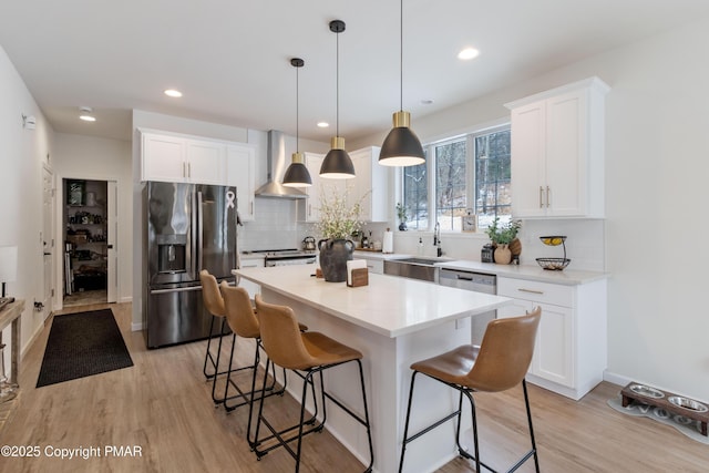 kitchen featuring wall chimney exhaust hood, white cabinetry, stainless steel appliances, and a kitchen island