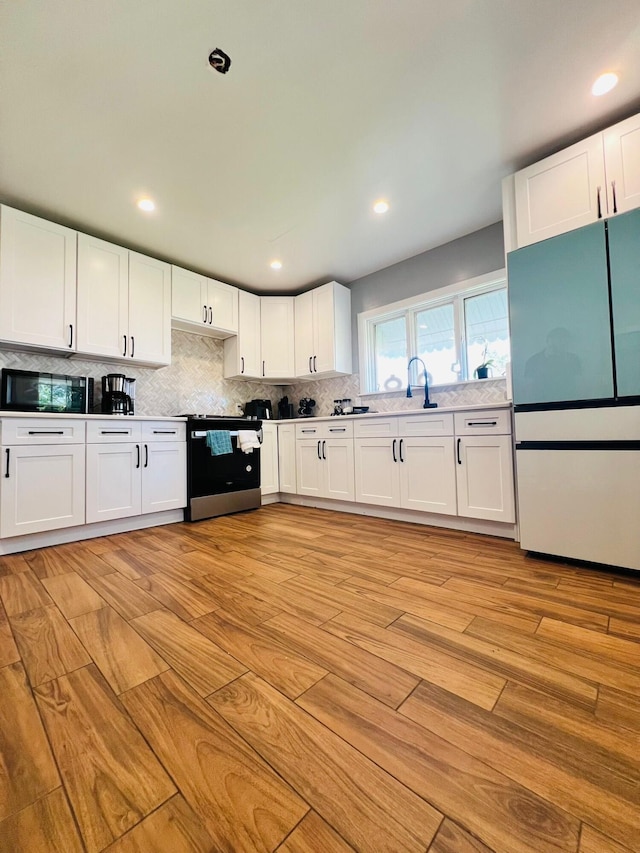 1116 Diamond Ave, Scranton, PA 18508 - kitchen with range with electric stovetop, freestanding refrigerator, light wood-style flooring, decorative backsplash, and white cabinetry