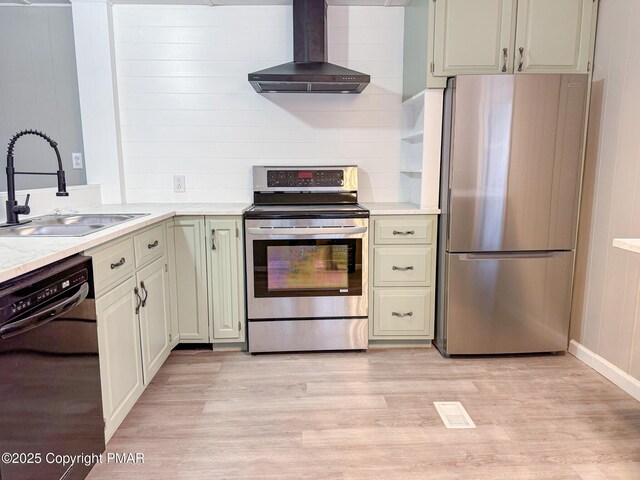 kitchen featuring appliances with stainless steel finishes, wooden walls, sink, light hardwood / wood-style floors, and wall chimney range hood